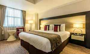 Et hotelværelse med en stor seng, dekorative puder, lamper og møbler. (AI-genereret tekst)