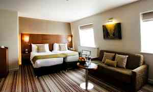 Hotelværelse med to enkeltsenge og en sofa. (AI-genereret tekst)