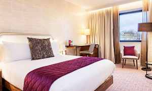 Et hotelværelse med en dobbeltseng, et skrivebord og en stol, ved siden af et vindue. (AI-genereret tekst)