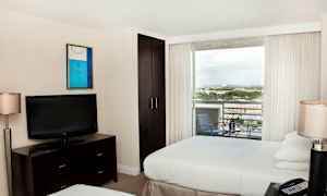 Et hotelværelse med to senge, et fjernsyn på en kommode, et skab og en altan med udsigt. (AI-genereret tekst)