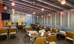 Et restaurantområde med ovenlysvinduer, borde og stole samt farverige hængelamper. (AI-genereret tekst)