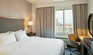 Et hotelværelse med en stor seng, et skrivebord med stol og udsigt gennem et vindue. (AI-genereret tekst)