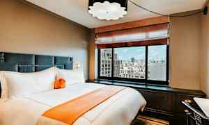 Et elegant hotelværelse med en seng, store vinduer og udsigt over byen. (AI-genereret tekst)