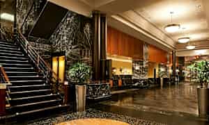 Billede af hotellets lobby med marmorgulv, en trappe, sofaer og plantearrangementer. (AI-genereret tekst)