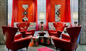 Et stilfuldt indrettet rum med røde lænestole, metalliske borde og lamper samt røde gardiner og moderne spejle på væggene. (AI-genereret tekst)