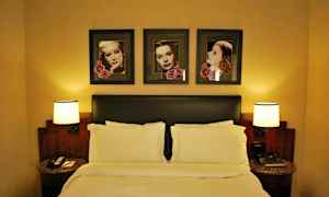 Hotelværelse interiør med en dobbeltseng, to natborde med lamper og billeder over sengen. (AI-genereret tekst)