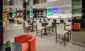 Interiør af en moderne bar med høje stole ved runde borde og en bardisk i baggrunden. (AI-genereret tekst)