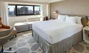 Et hotelværelse med en stor seng og udsigt mod byen gennem vinduet. (AI-genereret tekst)