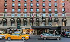En murstensbygning med markiser over indgange, trafik med biler og taxaer på gaden. (AI-genereret tekst)