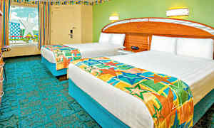 Et hotelværelse med to enkeltsenge dækket med farverige sengetæpper. Væggene er malet grønne, og der er et vindue med udsigt til en stjerneformet konstruktion. (AI-genereret tekst)