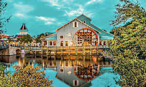 Bygning med et stort hjul ved vandet, omgivet af træer og vegetation. (AI-genereret tekst)