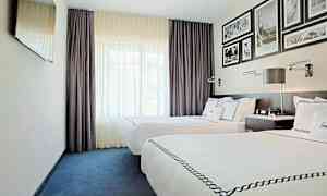 Et hotelværelse med to enkeltsenge med hvidt sengelinned og dekorative sengetæpper. Værelset har mørkelilla gardiner, et vægmonteret TV og indrammede billeder på væggen over sengegavlen. (AI-genereret tekst)