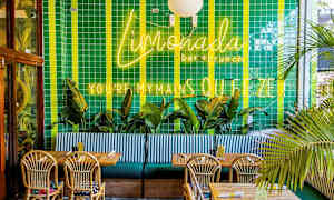 Restaurantinteriør med grønne flisebelagte vægge, neonskilte, palmer, træborde og flettede stole. (AI-genereret tekst)