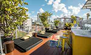 En terrasse med liggestole, puder og grønne planter. Der er en gul bardisk med taburetter ved siden af. (AI-genereret tekst)