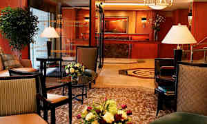 Et smagfuldt indrettet hotellobbyområde med møblerede siddeområder, interiørdetaljer, blomsterarrangementer og receptionen i baggrunden. (AI-genereret tekst)