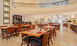 Elegant restaurant med borde og stole i træ, dekoreret med røde servietter og blomster. Bar og lys indretning ses i baggrunden. (AI-genereret tekst)