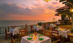 En udendørs restaurant med dækkede borde på en træterrasse ved havet under en farverig solnedgang. (AI-genereret tekst)