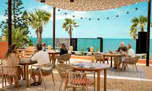 Udendørs servering med borde og stole foran en havudsigt. (AI-genereret tekst)