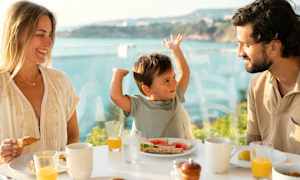 En familie spiser morgenmad ved et bord med udsigt over havet. (AI-genereret tekst)