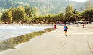 Sandstrand med mennesker, palmer og bjerge i baggrunden. (AI-genereret tekst)