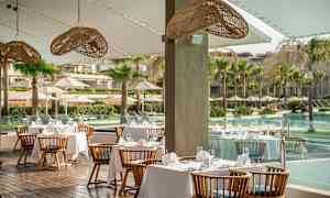 Restaurant med borde dækket med hvide duge og udsigt over pool og palmer. (AI-genereret tekst)