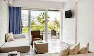 Et hotelværelse med sofa, lænestol og bord, med udsigt til en altan og grønne områder. (AI-genereret tekst)