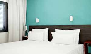 Hotelværelse med en opredt seng med hvidt sengetøj og blå væg. (AI-genereret tekst)