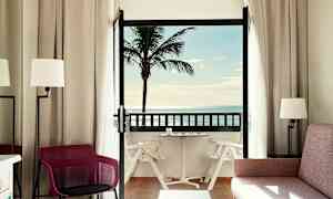 Et hotelværelse med balkon, der viser en palme og havudsigt. (AI-genereret tekst)