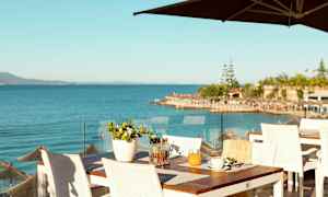 Udsigt over havet fra en restaurantterrasse med hvide borde og stole. (AI-genereret tekst)