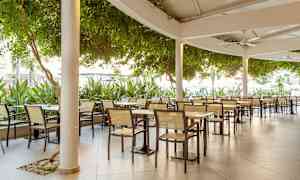 Billede af en udendørs restaurant med borde og stole under tag. (AI-genereret tekst)