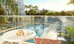 Udsigt fra en terrasse der viser en pool med solsenge og parasoller omgivet af grønne områder. (AI-genereret tekst)