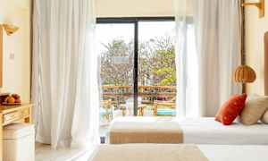 Et hotelværelse med dobbeltsenge og en glasdør, der fører ud til en altan. (AI-genereret tekst)