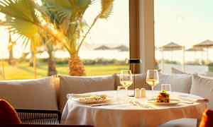 Et opdækket bord på en restaurant med mad og glas og en solrig udsigt med palmer. (AI-genereret tekst)