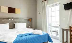 Et hotelværelse med en dobbeltseng, blåt sengetæppe og hvidt sengetøj. (AI-genereret tekst)