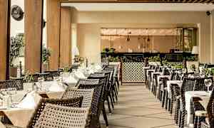 Udendørsservering med opdækkede borde og kurvestole, omgivet af grønne planter og moderne indretning. (AI-genereret tekst)