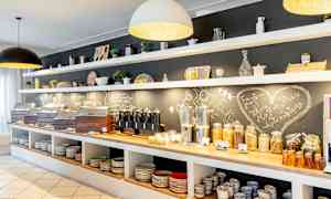 Morgenmadsbuffet med brød, kornprodukter, pålæg og drikkevarer. Hylder med porcelæn ovenover. (AI-genereret tekst)