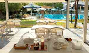 Et udendørs område med borde og stole, hvor poolområdet kan ses i baggrunden. (AI-genereret tekst)