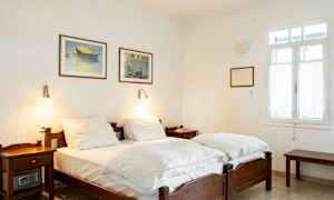 Et soveværelse med to enkeltsenge, hvide vægge og malerier på væggen. (AI-genereret tekst)