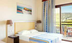 Et hotelværelse med en seng, oplyst med naturligt lys fra en balkon. (AI-genereret tekst)