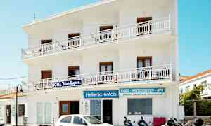 Hvid bygning med skilte for hotel og udlejning af køretøjer. Scootere og en bil er parkeret foran. (AI-genereret tekst)