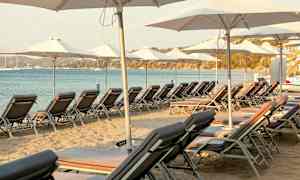 Solsenge og parasoller opstillede på sandstrand ved havet. (AI-genereret tekst)