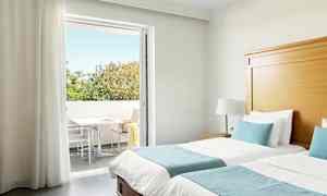 Hotelværelse med to enkeltsenge, blåt sengetøj og direkte adgang til en altan med træer i baggrunden. (AI-genereret tekst)