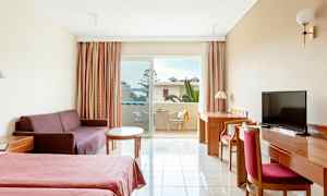 Et hotelværelse med to senge, en sofa, et bord, et skrivebord med stol og en altan med udsigt. (AI-genereret tekst)