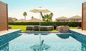 En swimmingpool med liggestole og en parasol i baggrunden. (AI-genereret tekst)