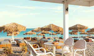 Udsigt over en sandstrand med parasoller og solsenge, set fra en siddeplads med bord og stole. (AI-genereret tekst)