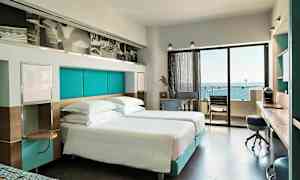 Moderne hotelværelse med dobbeltsenge og udsigt over havet fra balkonen. (AI-genereret tekst)