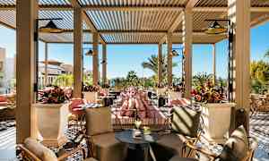 Udendørs loungeområde med siddepladser og planter, mod en baggrund af solrigt vejr. (AI-genereret tekst)