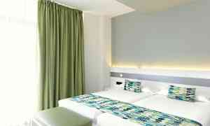 Et hotelværelse med to enkeltsenge, grønne gardiner og matchende sengedekorationer. (AI-genereret tekst)