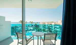 Udsigt fra en altan med to stole og et bord mod havet og en hotelpool. (AI-genereret tekst)