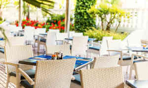 Udendørs servering med hvide flettede stole og dækkede borde med blå bordskånere. (AI-genereret tekst)